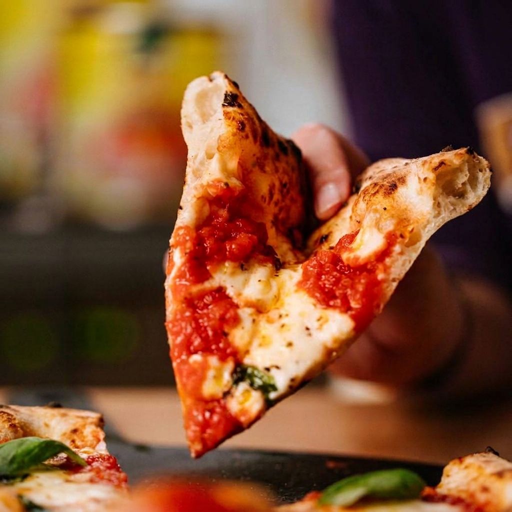 Ein Stück Margherita wird von einer Hand angehoben, der Käse zieht Fäden