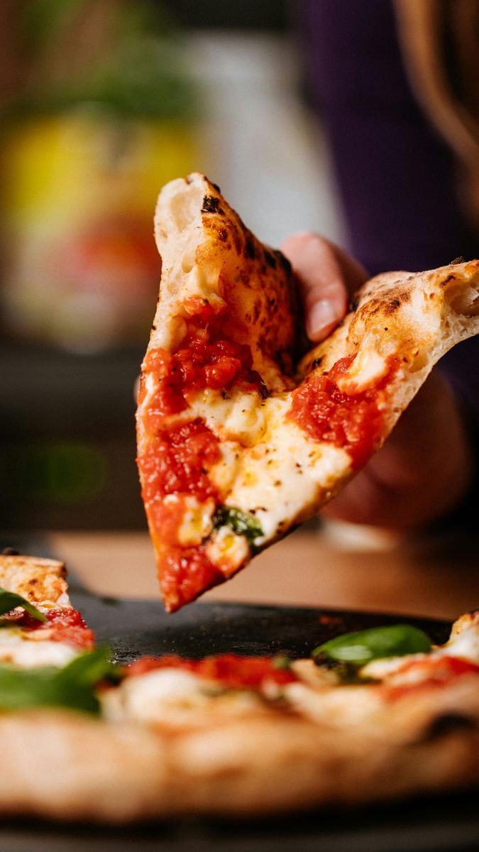 Ein Stück Pizza wird angehoben, der Käse zieht Fäden